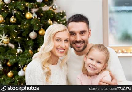 family, winter holidays and people concept - happy mother, father and little daughter at home over christmas tree background. happy family at home over christmas tree