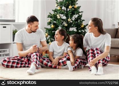 family, winter holidays and people concept - happy mother, father and two daughters sitting under christmas tree at home. happy family sitting under christmas tree at home