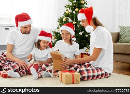 family, winter holidays and people concept - happy mother, father and two daughters in santa hats opening christmas gifts at home. happy family opening christmas gifts at home