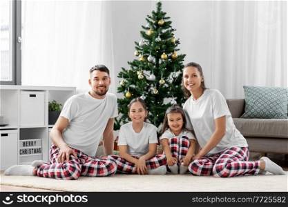 family, winter holidays and people concept - happy mother, father and two daughters sitting under christmas tree at home. happy family sitting under christmas tree at home