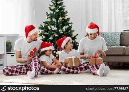 family, winter holidays and people concept - happy mother, father and two daughters in santa hats opening christmas gifts at home. happy family opening christmas gifts at home