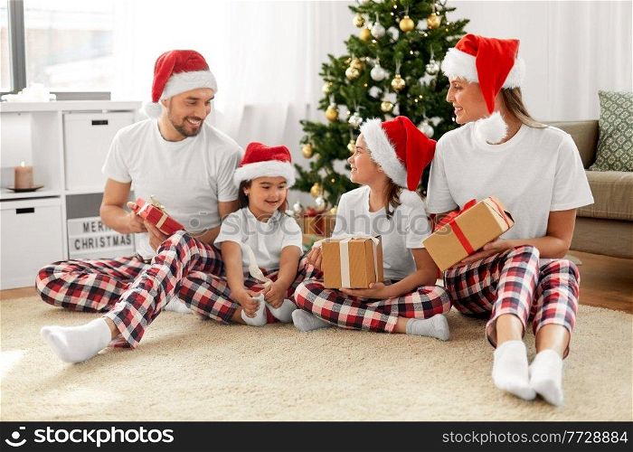 family, winter holidays and people concept - happy mother, father and two daughters in santa hats with christmas gifts at home. happy family with christmas gifts at home