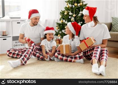 family, winter holidays and people concept - happy mother, father and two daughters in santa hats with christmas gifts at home. happy family with christmas gifts at home