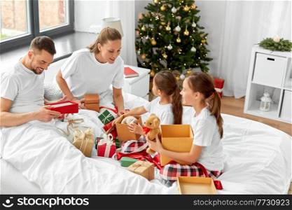 family, winter holidays and people concept - happy mother, father and two daughters opening christmas gifts in bed at home. happy family with christmas gifts in bed at home