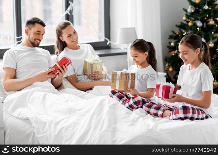 family, winter holidays and people concept - happy mother, father and two daughters in pajamas with christmas gifts in bed at home. happy family with christmas gifts in bed at home