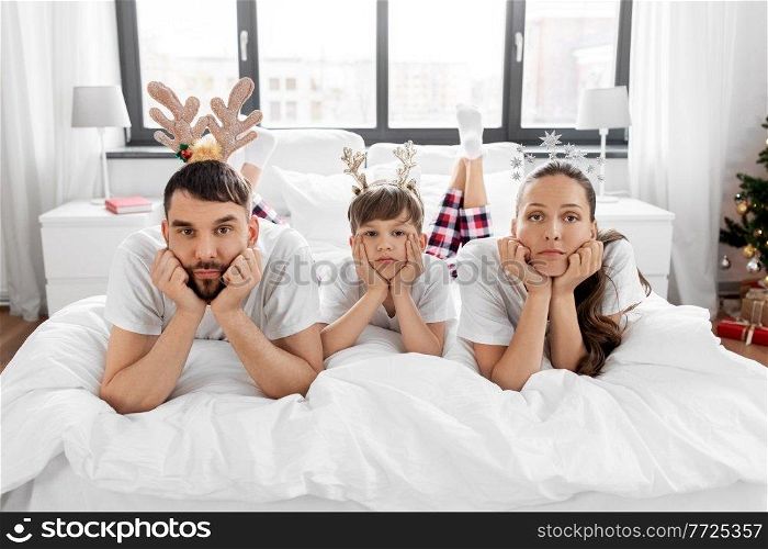 family, winter holidays and people concept - sad mother, father and little son in bed in christmas morning. sad family in bed in christmas morning