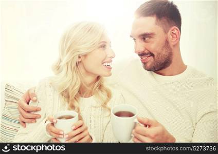 family, winter, holidays, love and people concept - happy couple with cups drinking tea and sitting on sofa at home. happy couple with cups drinking tea at home