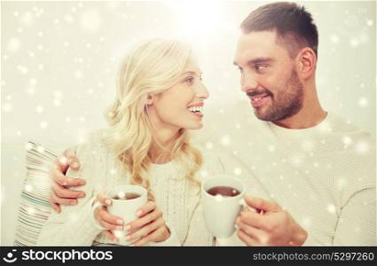 family, winter, holidays, love and people concept - happy couple with cups drinking tea and sitting on sofa at home. happy couple with cups drinking tea at home