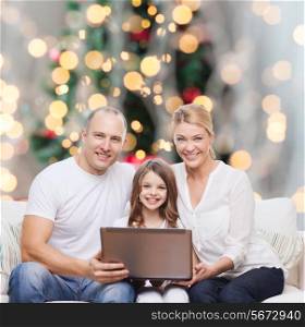 family, winter holidays, technology and people concept - smiling family with laptop computer over christmas tree lights background