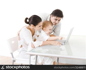Family with 2 years old baby boy sitting at the desk and using laptop computer.