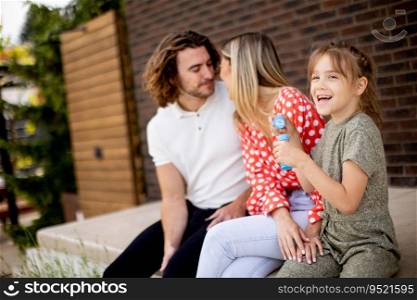 Family with a mother, father and daughter sitting outside on steps of a front porch of a brick house