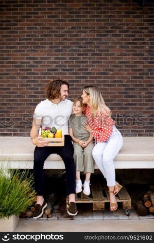 Family with a mother, father and daughter sitting outside on steps of a front porch of a brick house