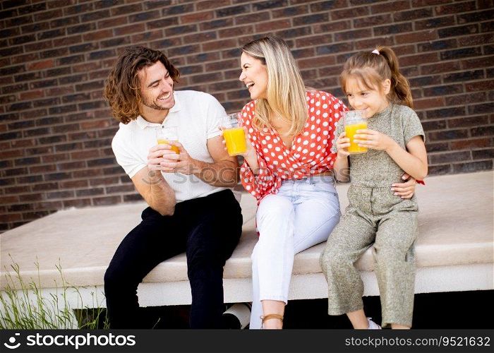 Family with a mother, father and daughter sitting outside on steps of a front porch of a brick house