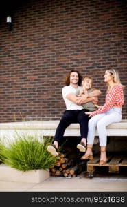 Family with a mother, father and daughter sitting outside on steps of a front porch of a brick house