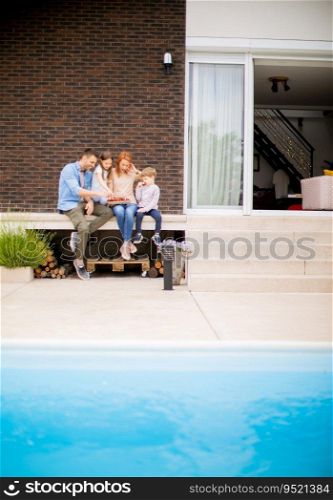 Family with a mother, father, son and daughter sitting outside by the swimming pool and eating strawberries
