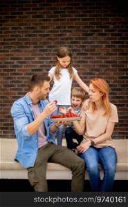 Family with a mother, father, son and daughter sitting outside on a steps of a front porch of a brick house and eating strawberries