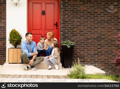 Family with a mother, father, son and daughter sitting outside on steps of a front porch of a brick house