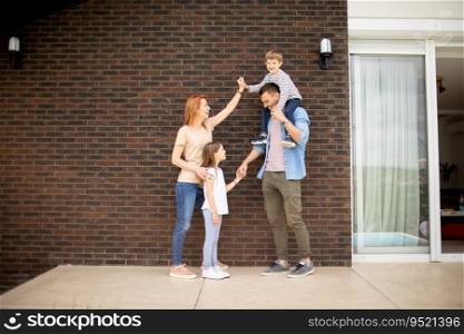 Family with a mother, father, son and daughter standing by the wall of a brick house