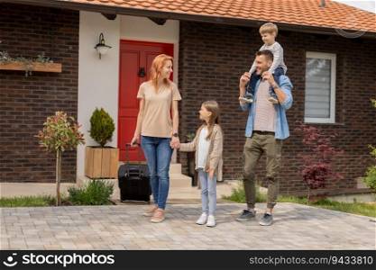 Family with a mother, father, son and daughter walking with  abaggage outside on the front porch of a brick house