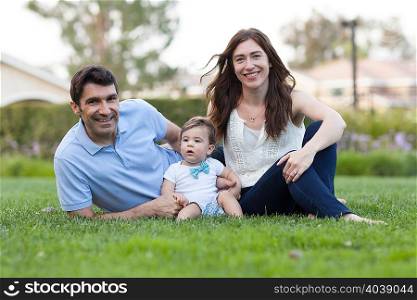 Family with baby boy sitting on grass looking at camera smiling