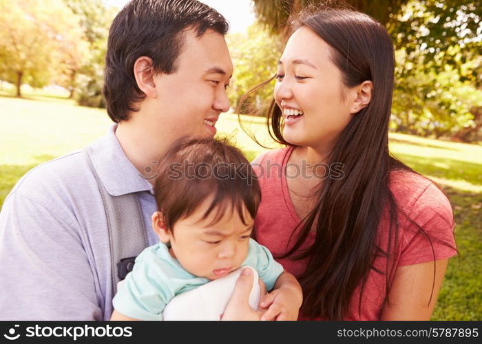 Family With Baby In Carrier Walking Through Park