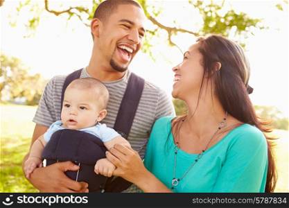 Family With Baby Son In Carrier Walking Through Park