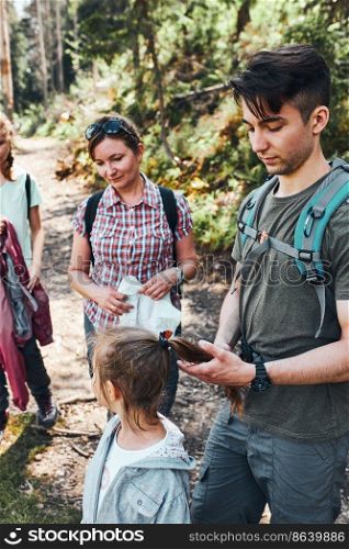 Family with backpacks hiking in a mountains actively spending summer vacation together walking down a forest path. Active people spending time outdoors in a forest. Family with backpacks hiking in a mountains actively spending summer vacation together