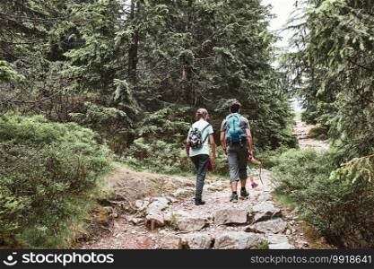 Family with backpacks hiking in a mountains actively spending summer vacation together walking on forest path talking and admiring nature mountain landscapes. Family with backpacks hiking in a mountains actively spending summer vacation together