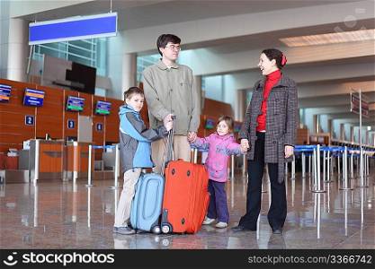 family with boy and girl standing in airport hall with two suitcases full body