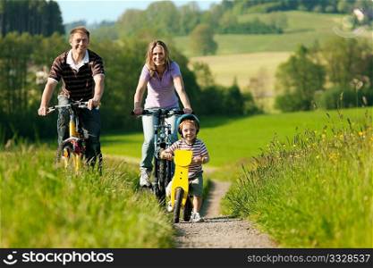 Family with boy child having a weekend excursion on their bikes on a summer day in beautiful landscape