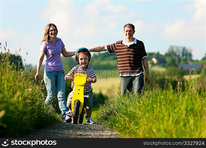 Family with boy child having a weekend excursion, the parents are walking while the son practices on a training bike