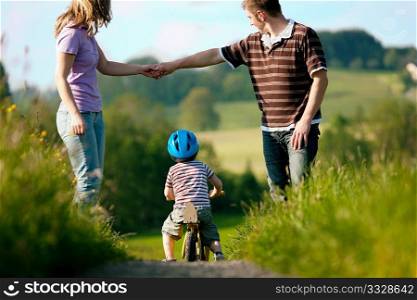 Family with boy child having a weekend excursion, the parents are walking while the son practices on a training bike