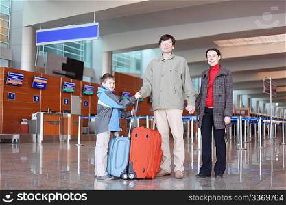 family with boy standing in airport hall with suitcases full body looking at camera