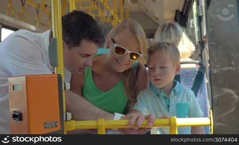 Family with child riding in city bus. Father showing the son how smartwatch works and allows him to use it