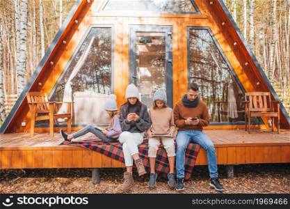 Family with children at autumn day, each with their own gadget outdoors. Happy family sitting on the terrace of their house in autumn