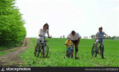 Family with children having a weekend excursion on their bikes. Father helping child learn to ride a bike
