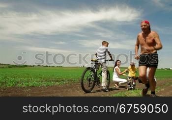 family with children having a weekend excursion on their bikes, senior man running.