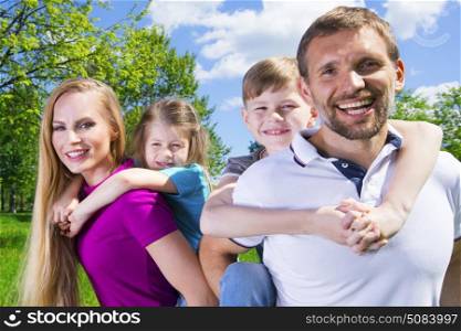 Family with children in park. Happy family portrat, couple giving two young children piggyback rides smiling in summer park