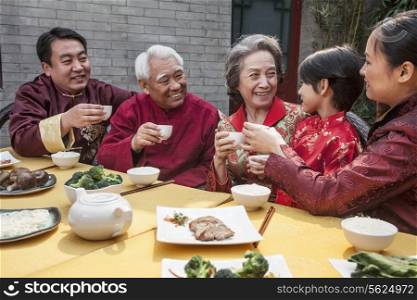 Family with cups raised toasting over a Chinese meal