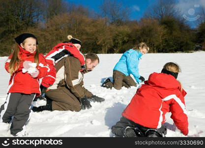 Family with kids having a snowball fight in winter on top of a hill in the snow