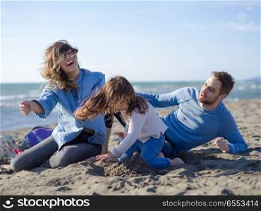 Family with little daughter resting and having fun at beach during autumn day. Young happy family enjoying vecation during autumn day