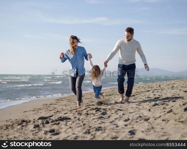 Family with little daughter resting and having fun at beach during autumn day. Young happy family enjoying vecation during autumn day