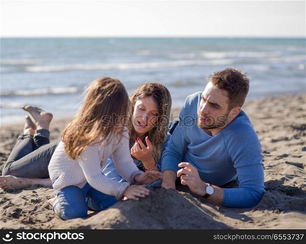 Family with little daughter resting and having fun at beach during autumn day. Young family enjoying vecation during autumn day
