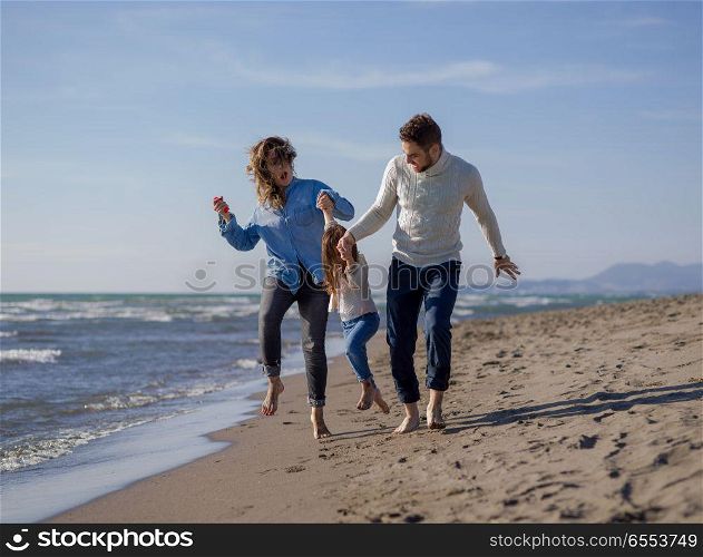 Family with little daughter resting and having fun at beach during autumn day. Young family enjoying vecation during autumn day