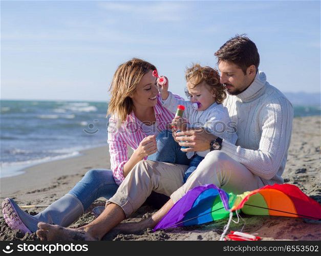 Family with little daughter resting and having fun making soap bubble at beach during autumn day. Young family enjoying vecation during autumn day