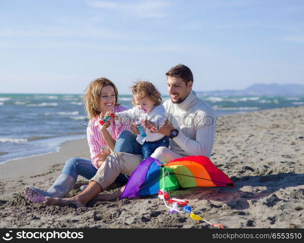 Family with little daughter resting and having fun making soap bubble at beach during autumn day. Young family enjoying vecation during autumn day