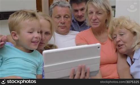 Family with parents, son and grandparents watching something on touch pad ad smiling