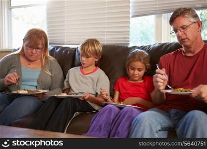 Family With Poor Diet Sitting On Sofa Eating Meal