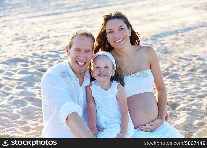 Family with pregnant mother on the beach sand happy in summer vacations