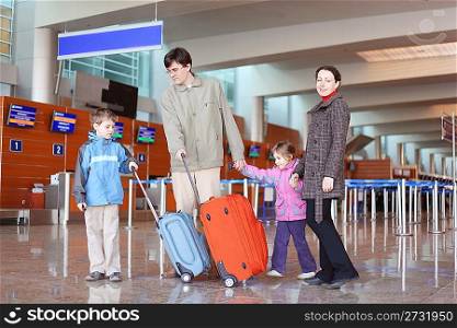 family with suitcases walking in airport hall